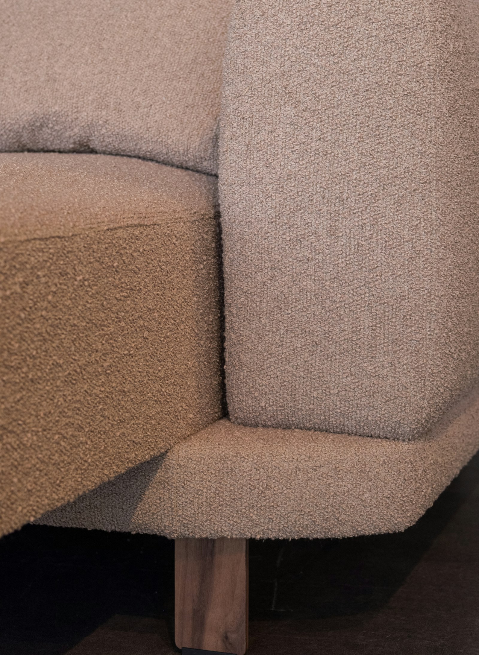 Close detail of a textured beige sofa on turned wooden legs.