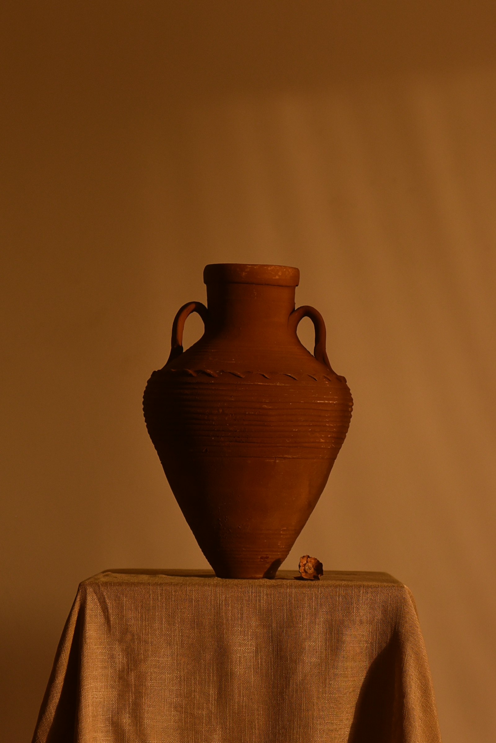 A tall handled terracotta amphora on a cloth-covered plinth in warm shade.